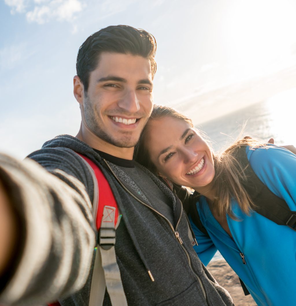Couple taking a selfie while hiking and watching the sunset from a cliff by the beach